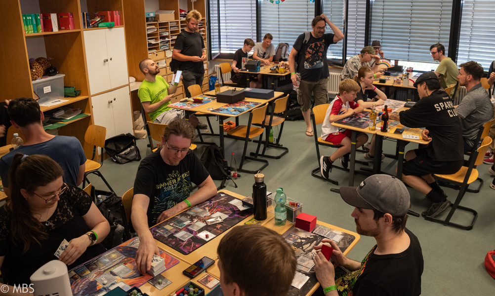 An zahlreichen Tischen spielen Besucher:innen Trading-Card-Games.
