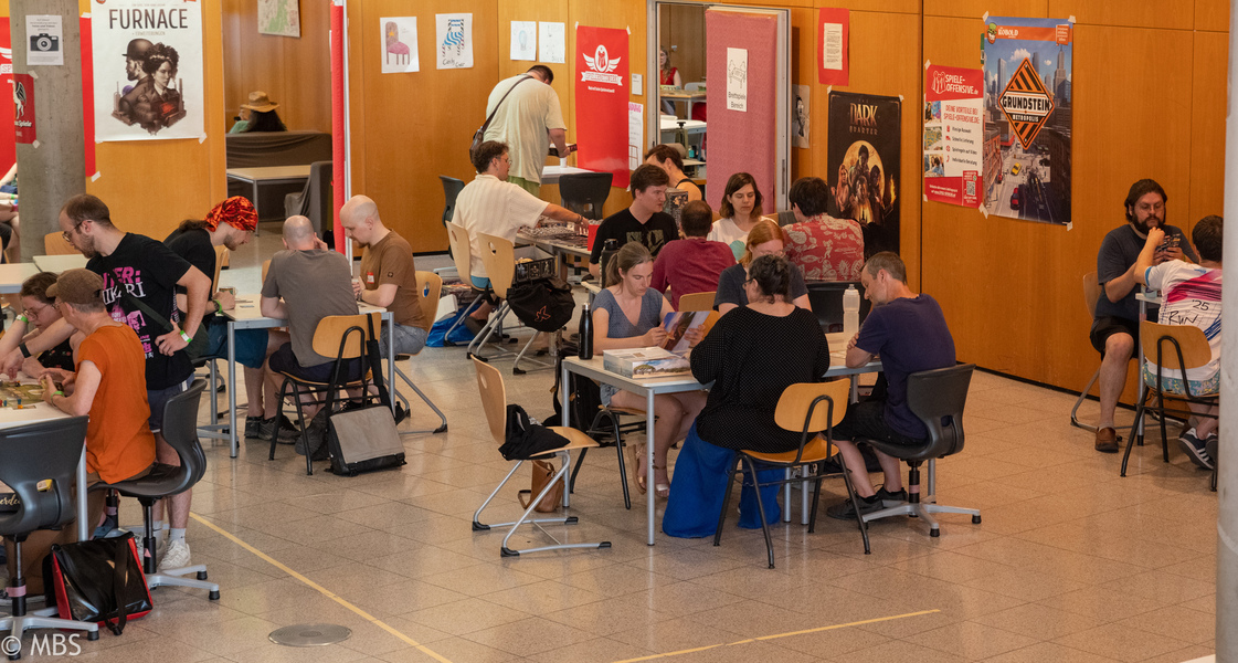 An zahlreichen Tischen Spielen Besucher:innen Brettspiele.